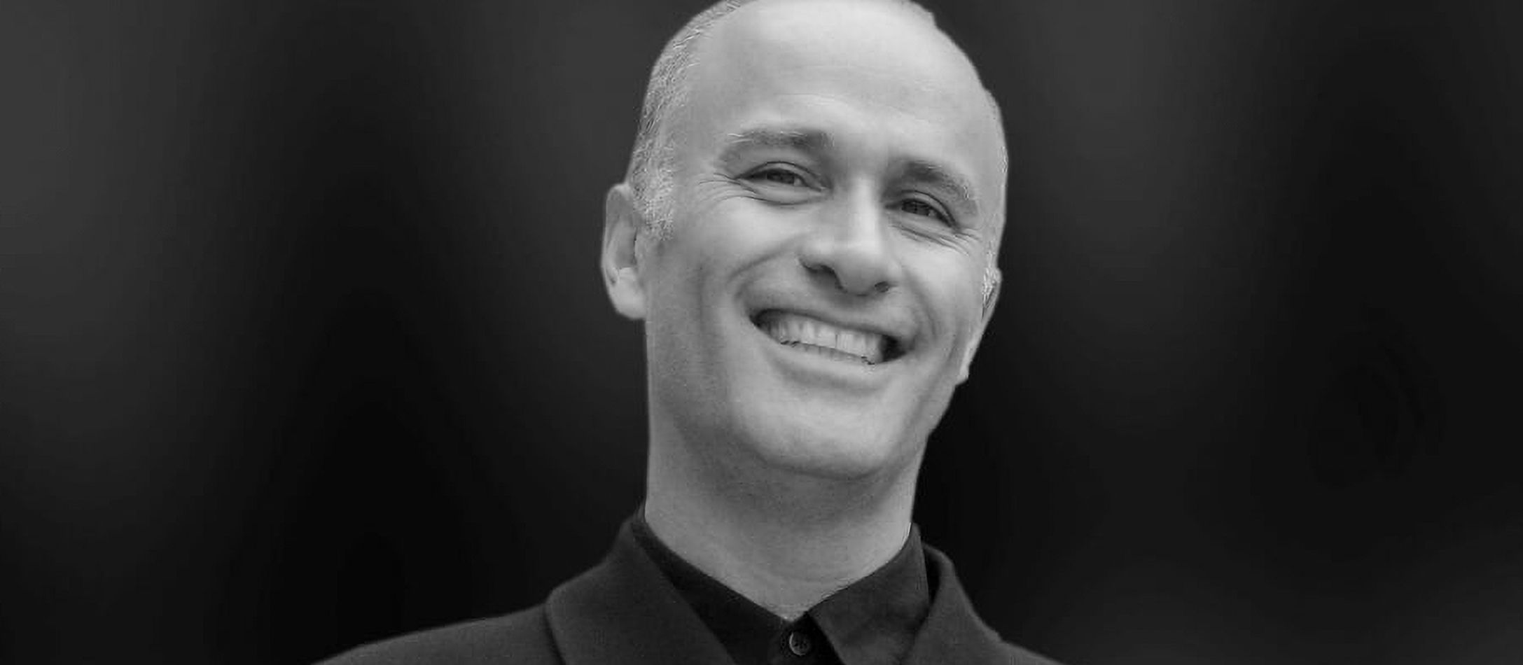 Nicholas Kok i sort/hvid står oprejst i sort klassisk, stilet efterårsjakke og smiler blidt med blottede hvide tænder.