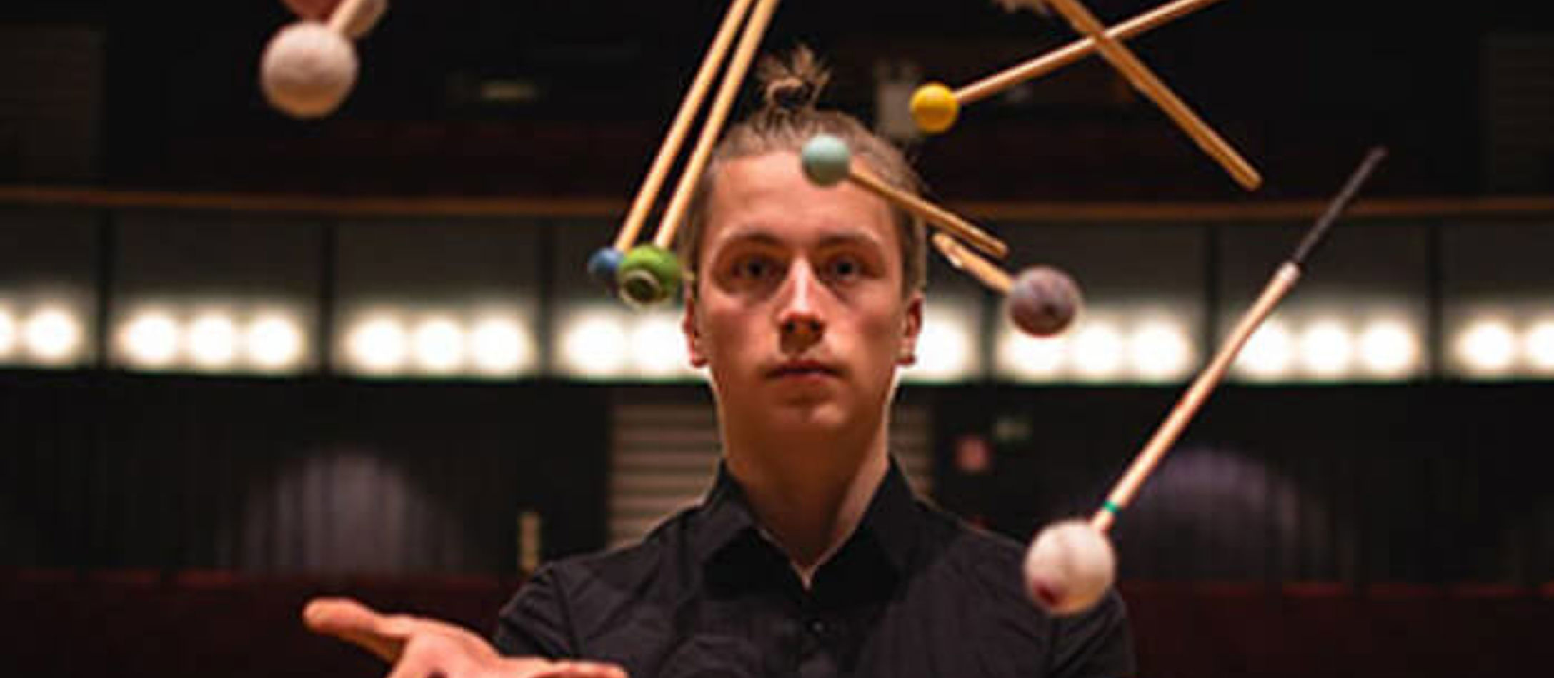 Kalle Hakosalo med manbun jonglerer med slagtøj i sort skjorte